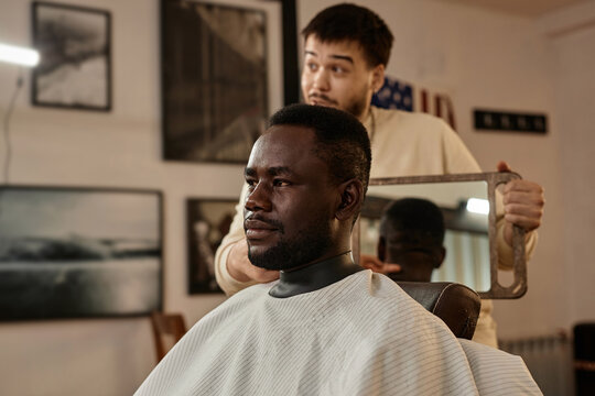 African American customer admiring his haircut in barber shop while barber holding the mirror
