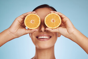 Happy woman, eyes and orange for natural vitamin C, skincare or diet against a blue studio background. Face of person smile with organic citrus fruit for nutrition, dermatology or healthy wellness