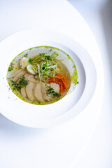 soup with meat and herbs in a white plate on the windowsill