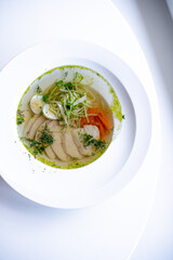 soup with meat and herbs in a white plate on the windowsill