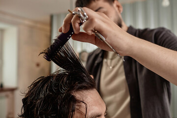 Fototapeta premium Close-up of barber cutting hair of customer with scissors and comb in barber shop
