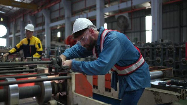 A team of factory technician use a wrench to inspect the conveyor belt of the metal sheet production machine.