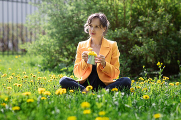 Happy free young woman sitting outdoors on field with flowers and green grass, enjoying spring