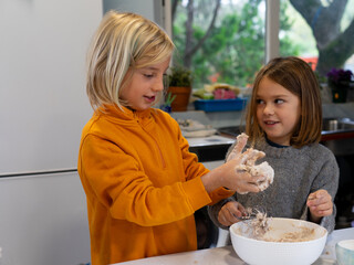 Two children cooking a pizza together in the kitchen at home