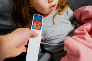 Measuring body temperature of child. Digital thermometer showing high fever body temperature