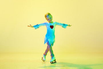 Artistic, talented little girl, child, adorable kid in costume dancing, training figure skating against yellow background in neon. Concept of childhood, figure skating sport, hobby, school, education