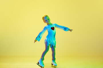 Fototapeta na wymiar Full-length of cute, beautiful adorable kid, little girl, dancing, performing figure skating against yellow background in neon. Concept of childhood, figure skating sport, hobby, school, education
