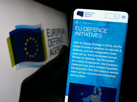Stuttgart, Germany - 10-17-2023: Person holding cellphone with webpage of EU institution European Defence Agency (EDA) in front of logo. Focus on center of phone display.