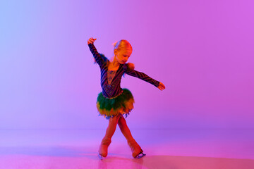 Beautiful, adorable little girl, child in stage costume dancing, performing figure skating against gradient pink purple background in neon. Concept of childhood, figure skating sport, hobby, school - obrazy, fototapety, plakaty
