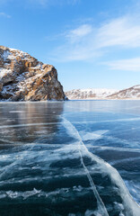 Beautiful winter landscape of frozen Baikal Lake in cold sunny February day. Natural background with blue ice with white cracks near coastal rocks. Winter ice travel and outdoor recreation