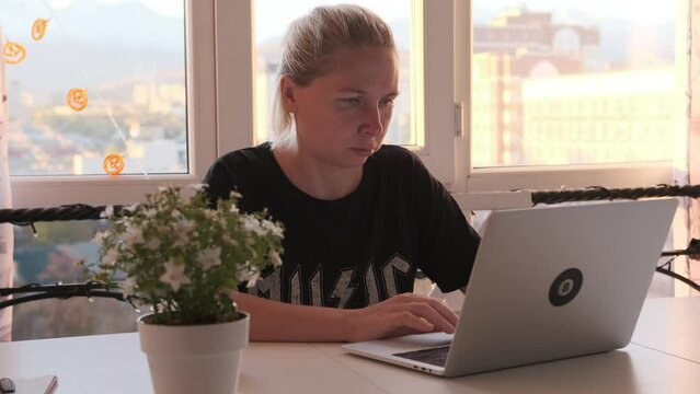 Focused young woman freelancer busy working on laptop computer at city office near flowers on table. Productivity and efficiency in workplace.