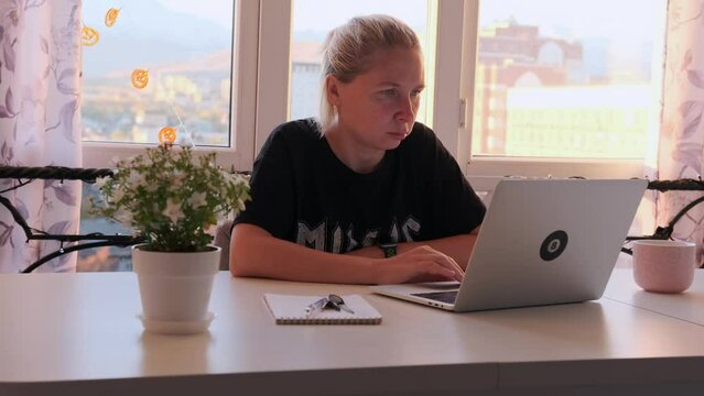 Girl passionate about project sits with laptop, browsing websites and reading articles. Student teaches lectures via the Internet at home in morning, sitting at table in cozy living room.