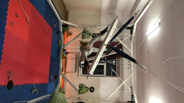 Orthopedic device for spinal traction. Woman swings on stretching machine, tied tropes near the ceiling above a trampoline. Stretching machine. 