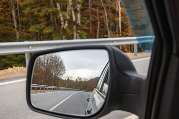 Fototapeta na wymiar Car rear view mirror. Beautiful scene of autumn trees and road in the mirror