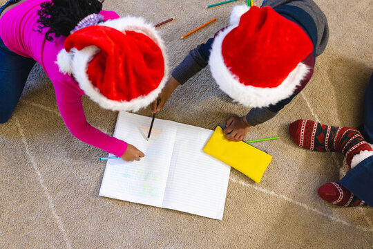 African american boy and girl, wearing christmas hat and drawing in notebook at home, copy space