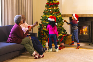 Happy african american grandparents and grandchildren and decorating christmas tree, copy space