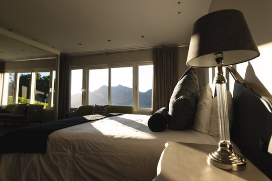 Interior of sunny domestic bedroom with bedside lamp, double bed and mountain views, copy space