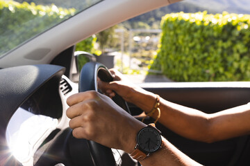 Hands of african american man on steering wheel, driving car on sunny day
