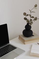 Laptop with blank screen, aesthetic black vase with eucalyptus branches, notebook with pencil and...