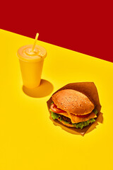 Tasty hamburger with beef sauces and vegetables with refreshing drinks against vivid red-yellow background. Concept of fast food, delivery.