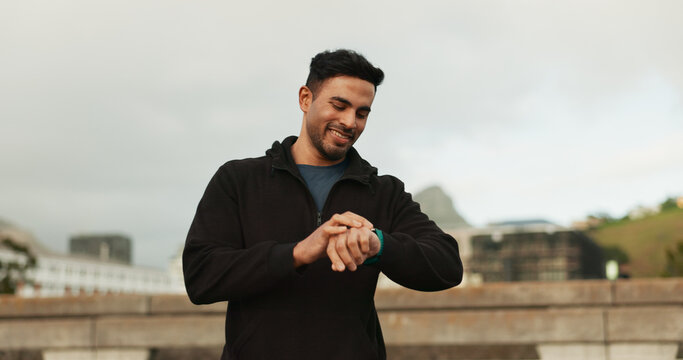 Smart watch, happy and man in city for exercise, cardio fitness and healthy training progress. Indian runner check stopwatch for timer, heart rate and workout performance, clock and results outdoor - Powered by Adobe