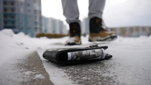 A lost wallet on the snowing asphalt with hundred dollar bills close-up and a random person finds it