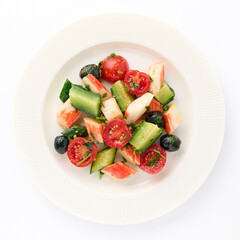 Healthy salad of crab sticks sliced vegetables cherry tomato, cucumber, olives on white plate on an isolated white background top view for your design. Healthy food. Protein, vitamins