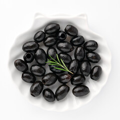 Delicious black olives in plate with olive tree sprig decoration isolated on white background top view for your design. Healthy eating, healthy fats for humans. Organic vegetable