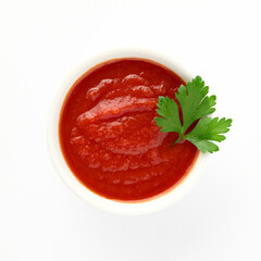 Red tomato ketchup sauce for meat dishes in plate isolated on white background decorated with green sprig of parsley for your design top view. Healthy eating