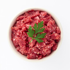 Fresh minced veal decorated with sprig of parsley in plate on an isolated white background top view...