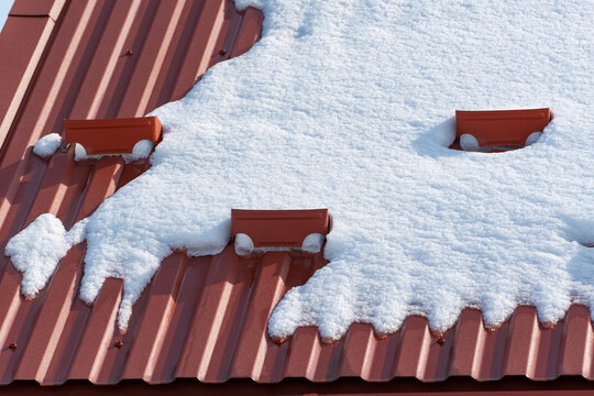 Snow guard system. Roof made of brown metal tiles covered with snow. Ice and snow retention