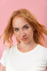 Confident look of a beautiful green-eyed woman with red hair. Attractive young woman on pink background. Close-up, vertical frame