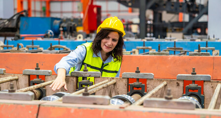 Senior female engineer manager wearing a hard hat and reflective safety vest inspects the maintenance of steel roof production line machinery in the factory.