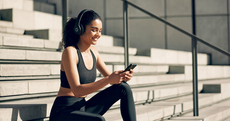 Runner woman, headphones and phone on stairs with music, smile and relax in city, workout and...