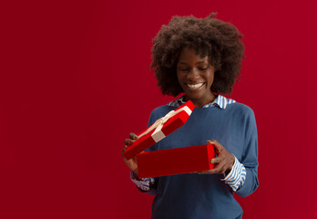 Beautiful African American woman with Christmas presents, smiling on red background 