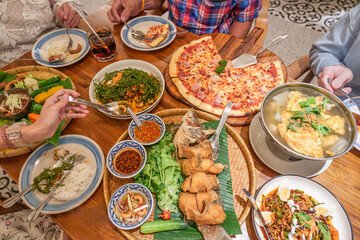 Dinner meal with Thai food as fried fish with spicy sauce, Spicy vegetable salad, Local vegetables with chili sauce and pizza bacon ham cheese on wooden table