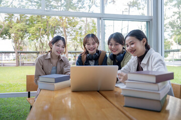 University students sitting together at table with book and laptop. Happy young people doing group study in college campus