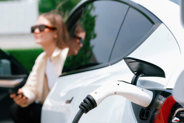 Young woman use smartphone to pay for electricity at public EV car charging station green city...