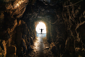Silhouette man standing on end of natural cave, underground tunnel and light shines