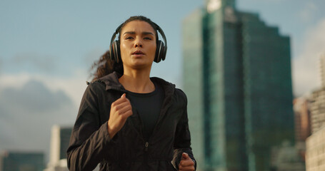 Fitness, music and a sports woman running in the city for health or cardio preparation of a marathon. Exercise, wellness or training and a young runner or athlete listening to audio with headphones