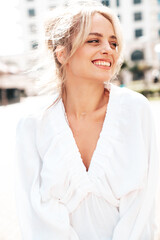 Portrait of young beautiful smiling woman in trendy summer white  dress. Sexy carefree woman posing in the street  background at sunset. Positive model outdoors at sunny day. Cheerful and happy