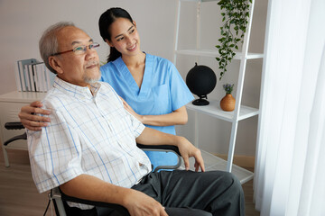 Fototapeta premium nurse or caregiver beside elderly man sitting on wheelchair and looking outside at home