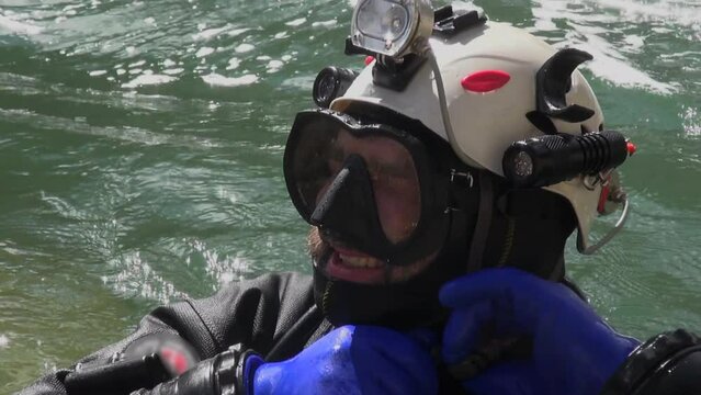 Closeup: Bearded tech scuba diver dons helmet in turbulent river water