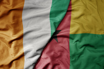 big waving national colorful flag of cote divoire and national flag of guinea bissau .