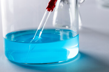 Close up of laboratory dish with blue liquid and copy space on grey background