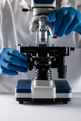 Vertical image hands of scientist in gloves using microscope and copy space on white background