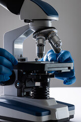 Vertical image hands of scientist in gloves using microscope and copy space on grey background