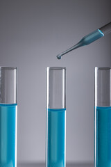 Vertical image of laboratory test tubes with blue liquid, pipette and copy space on grey background