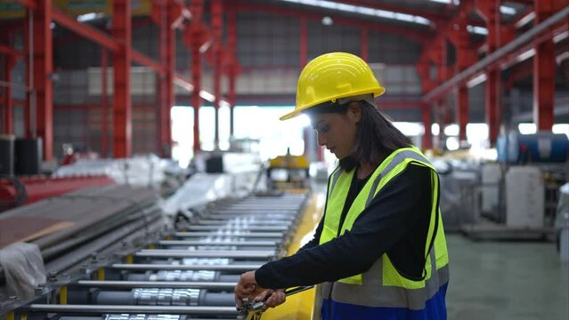 A female factory technician use a wrench to inspect the conveyor belt of the metal sheet production machine.
