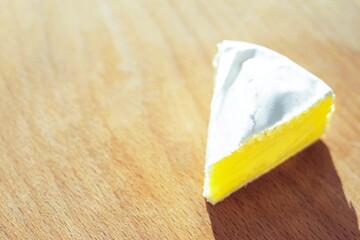 Camembert cheese triangular slice on a wooden sunny table. Copy space